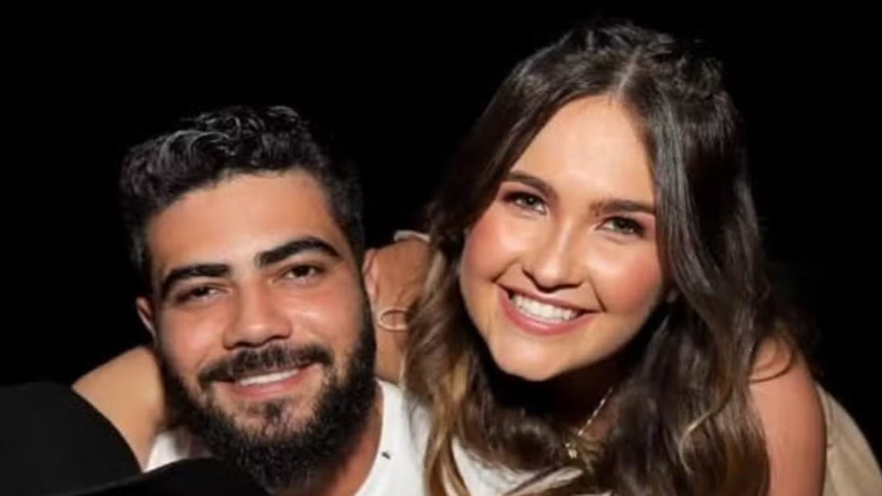 Homem e mulher sorrindo juntos em ambiente escuro com iluminação destacando seus rostos