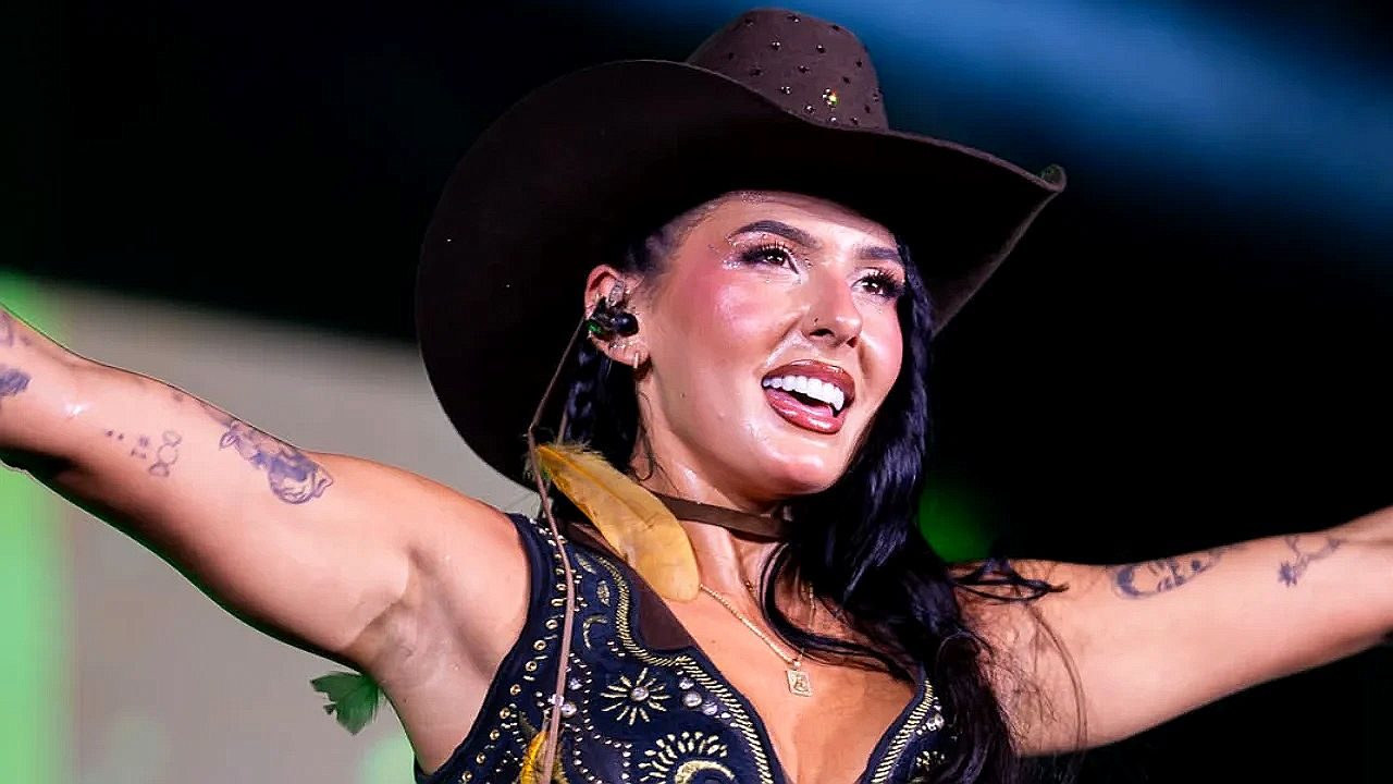 Ana Castela canta com chapéu de cowboy e braços abertos durante apresentação em show sertanejo ao vivo