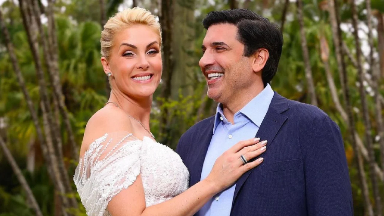 Ana Hickmann vestida de noiva ao lado de Edu Guedes com um terno azul e um fundo de árvores