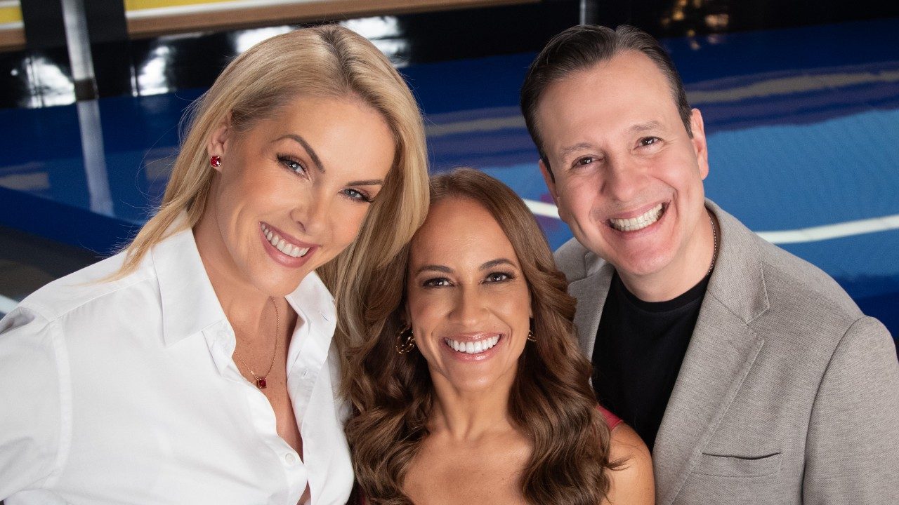 Ana Hickmann, Renata Alves e Celso Zucatelli sorriem juntos no estúdio do Hoje em Dia, Ana veste camisa branca, Renata tem cabelos ondulados e Celso usa paletó cinza-claro