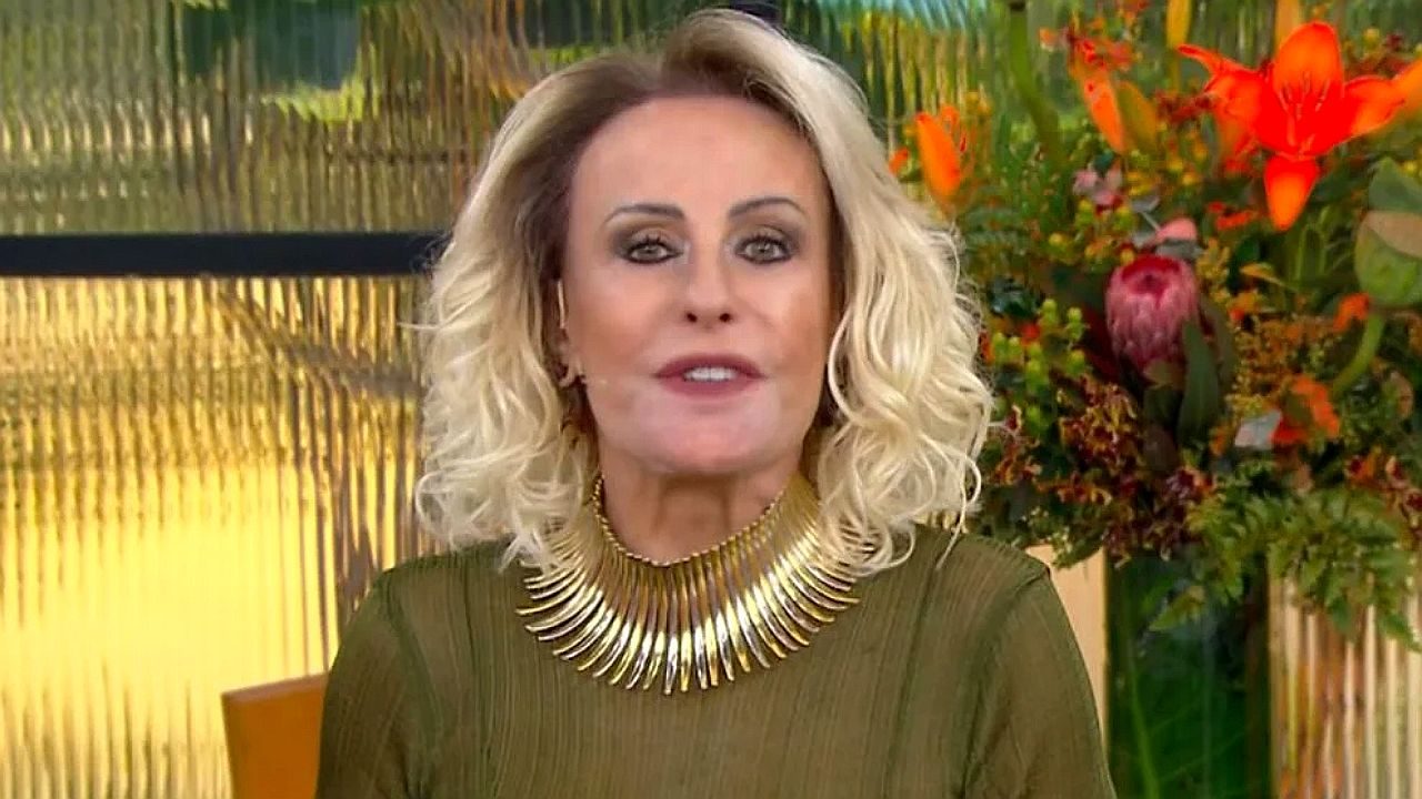 Ana Maria Braga fala no Mais Você usando vestido verde e colar dourado em estúdio com flores ao fundo