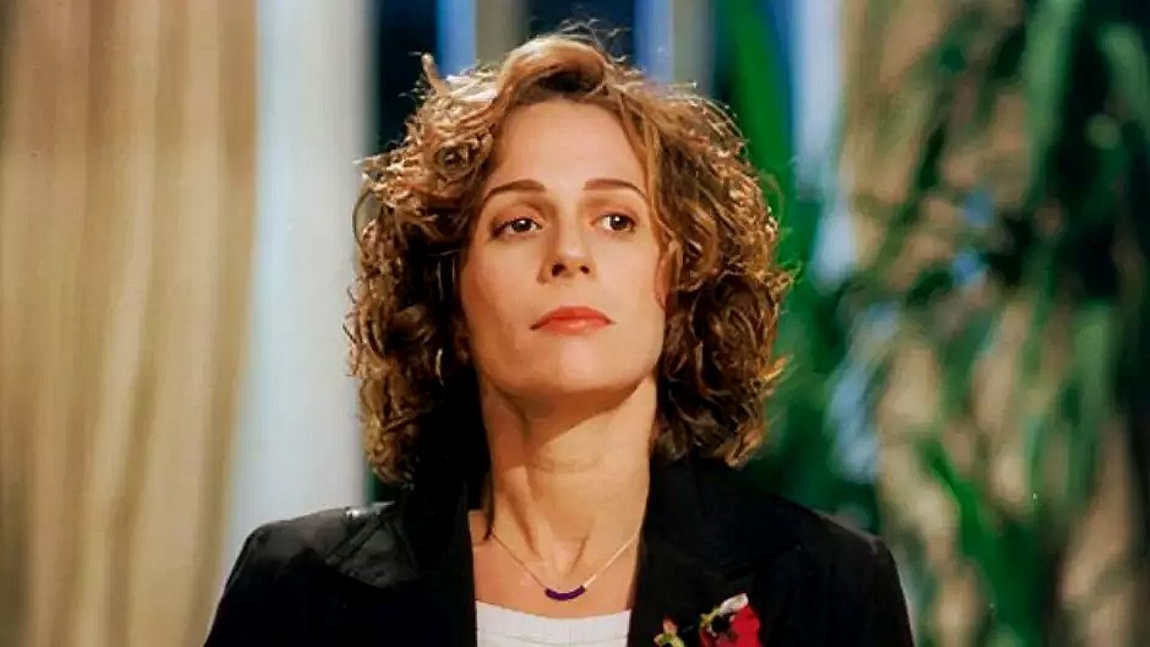 A atriz Andrea Beltrão em uma casa com um blazer preto e expressão séria