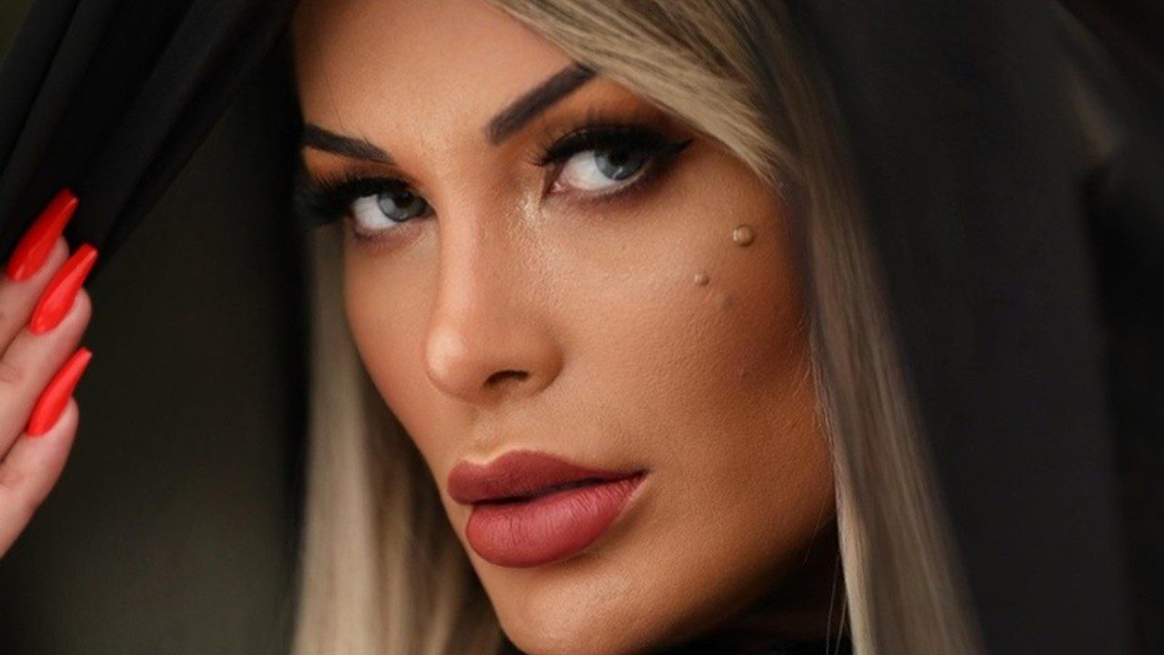 Andressa Urach em close com olhar direto usando maquiagem marcante e unhas longas vermelhas com detalhe no rosto visível