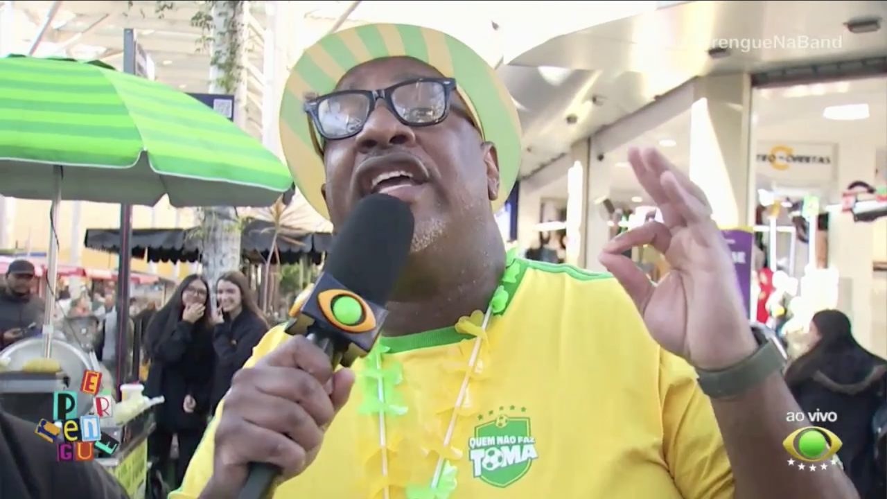 Ângelo Campos, de camiseta amarela, fala ao microfone em rua durante gravação do Perrengue na Band