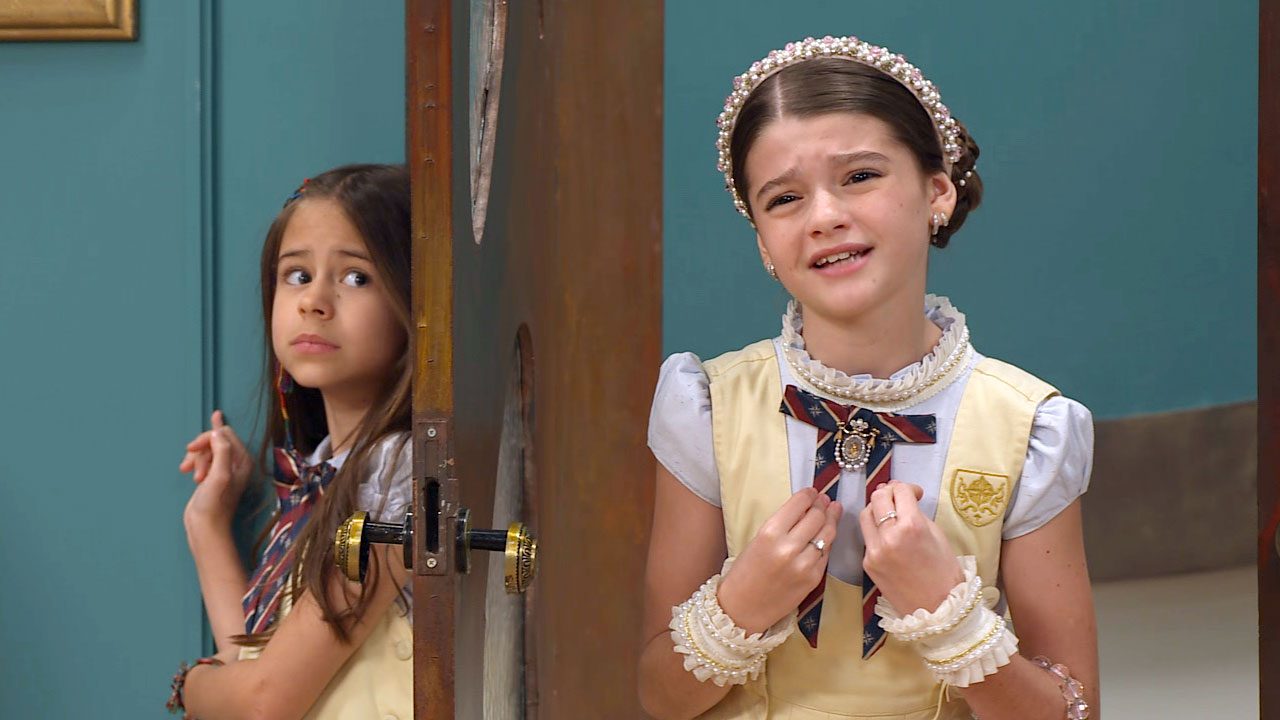 Anna (Mel Summers) e Lavínia (Juju Penido) usando uniforme escolar em cena de A Caverna Encantada, do SBT, com expressões preocupadas