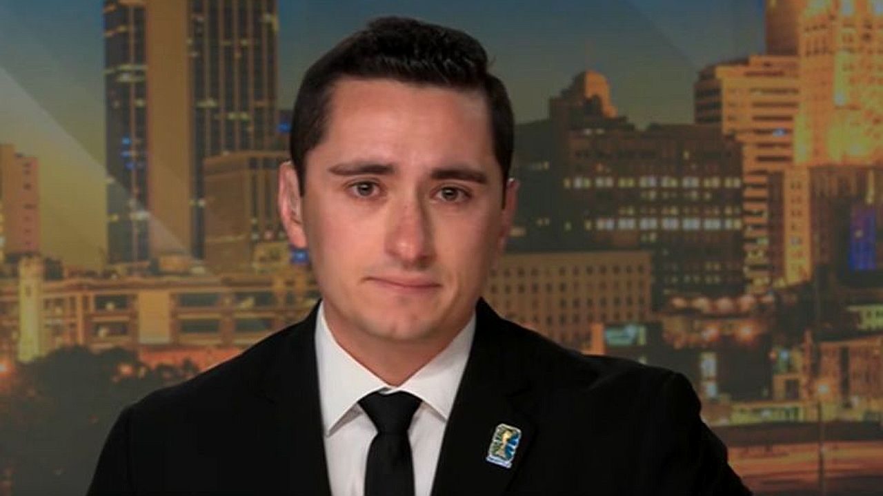 Samson Tamijani durante participação em telejornal com expressão emocionada diante de cenário urbano ao fundo