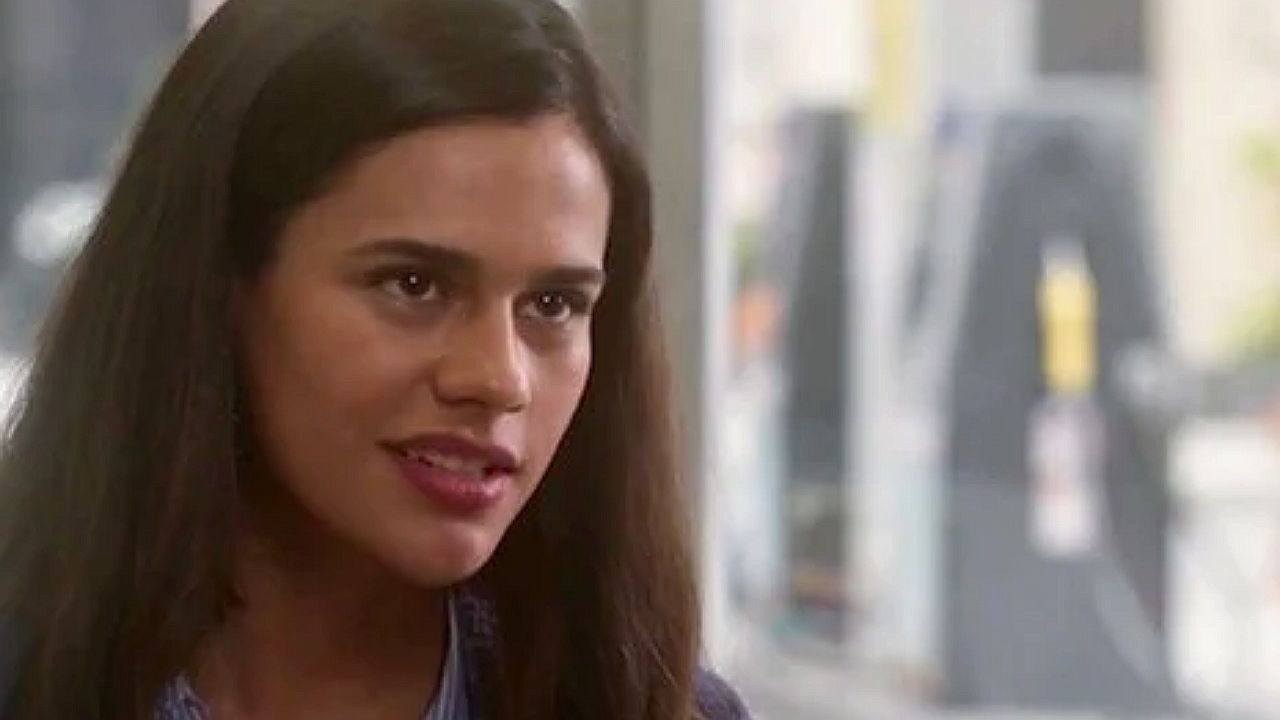 Atriz interpreta jovem determinada em cena de novela ambientada em escritório com expressão desafiadora