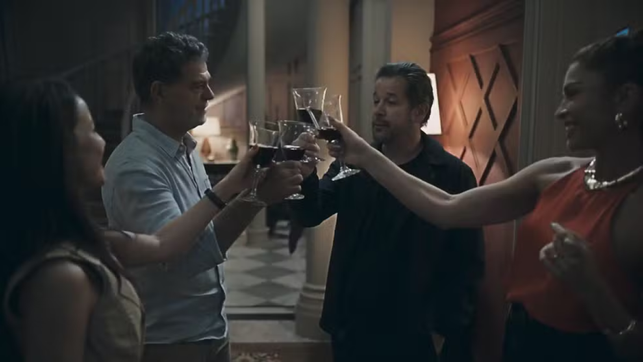 Quatro pessoas brindam com bebidas em uma cena escura