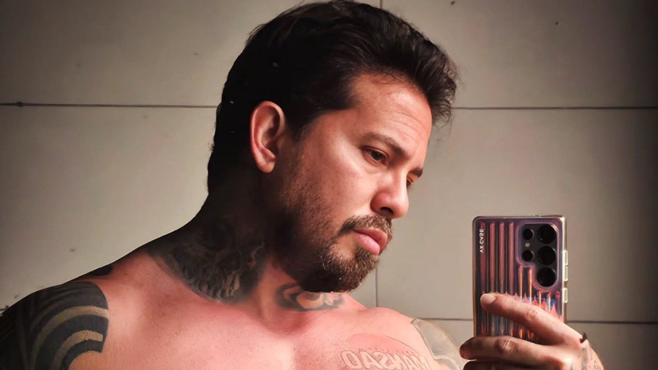 Arthur O Urso tira selfie sem camisa exibindo tatuagens no pescoço e braço em ambiente interno com espelho