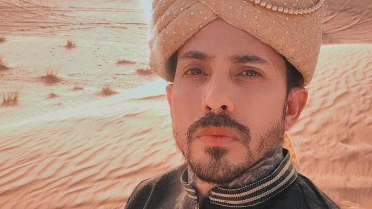 Arthur O Urso posa com turbante e roupa tradicional em cenário de dunas no deserto