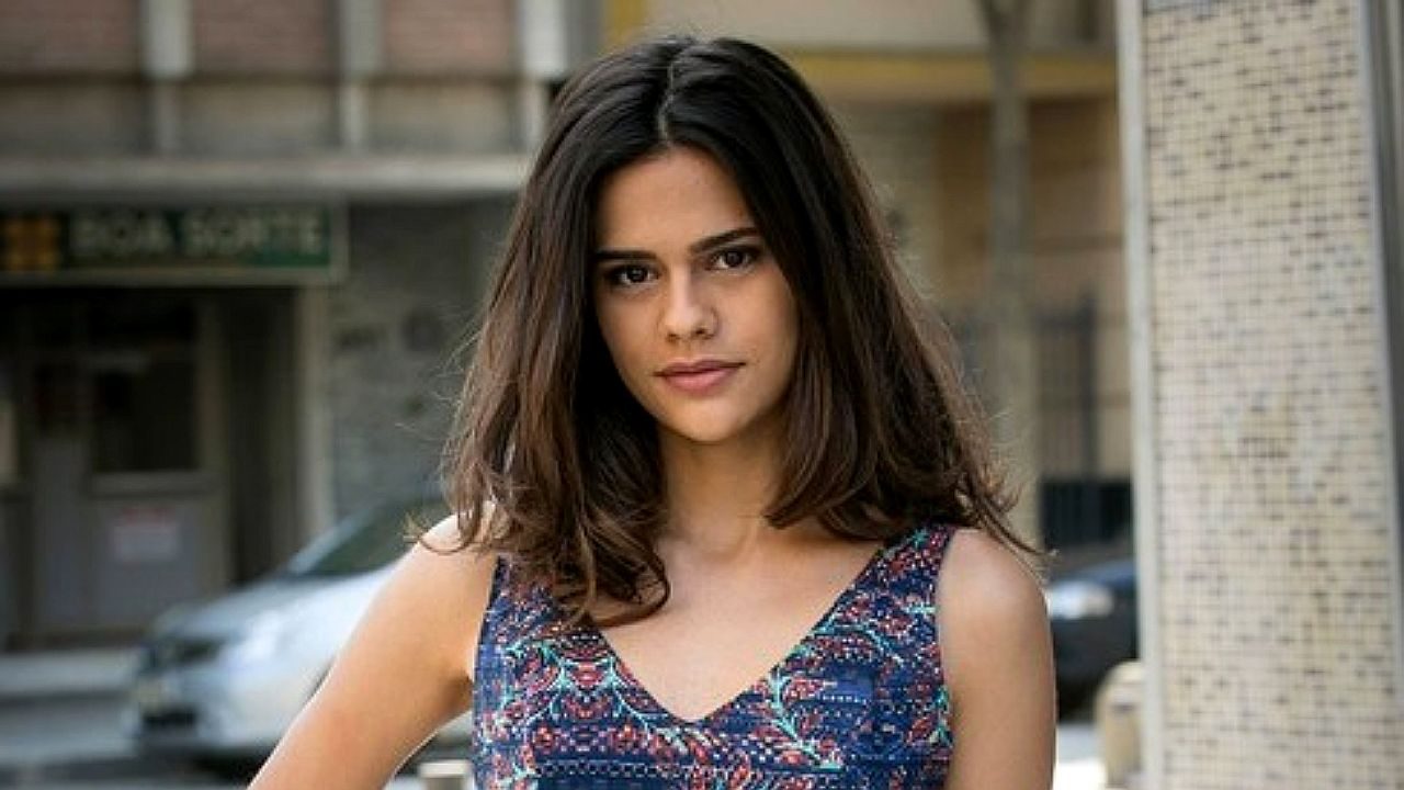 Aryanne Botelho posa em rua urbana com vestido estampado em foto promocional de personagem de novela brasileira