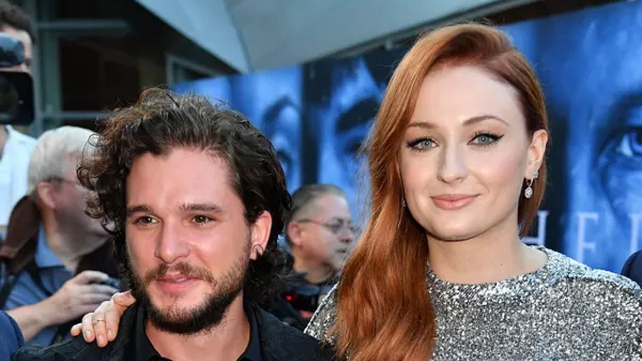 Kit Harington e Sophie Turner posam juntos em evento de estreia com fotógrafos e painel promocional da série ao fundo