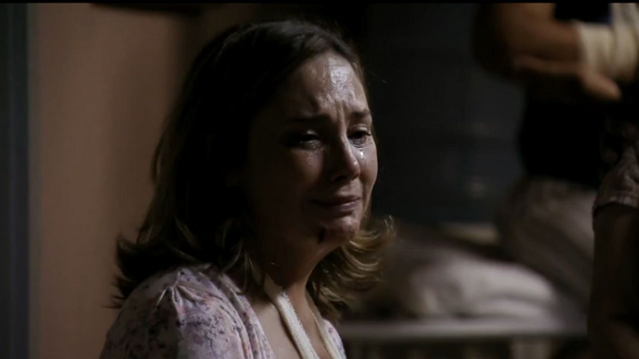 Mulher chora com lágrimas no rosto em cena dramática dentro de ambiente escuro