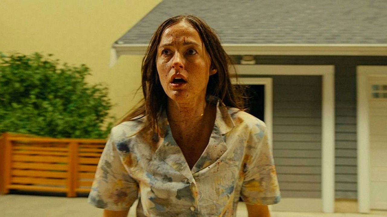 Mulher assustada e coberta de sujeira em frente a uma casa durante cena do filme de terror Backrooms