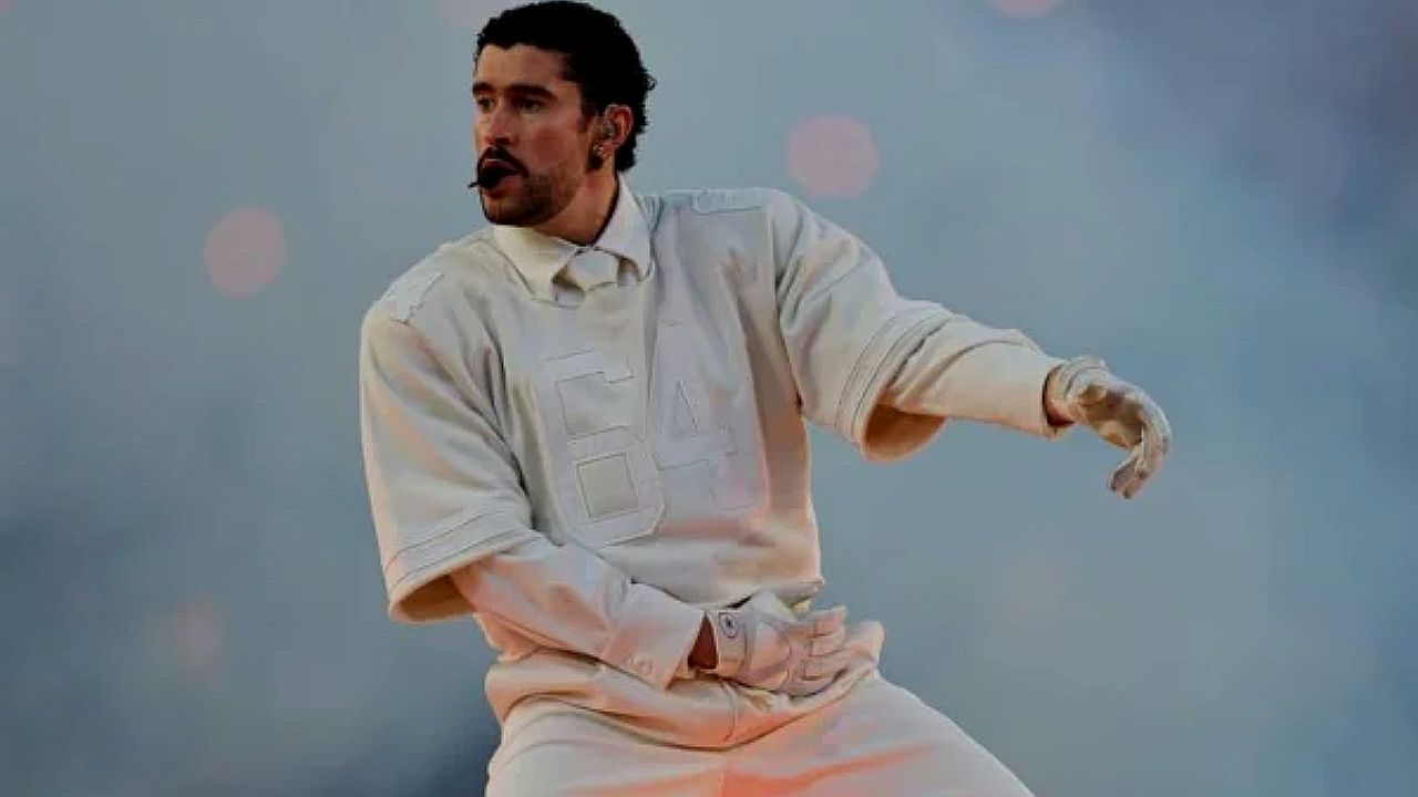Bad Bunny se apresenta com roupa branca e microfone headset durante show em palco iluminado