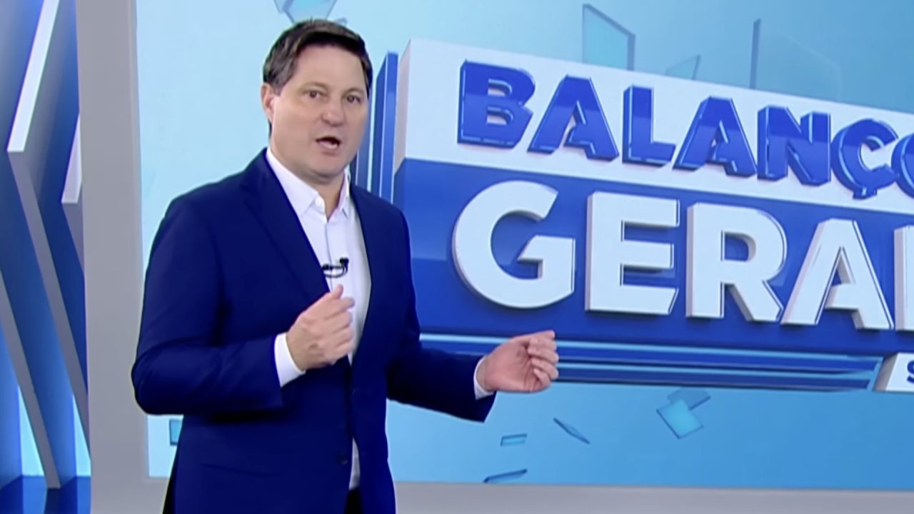 Eleandro Passaia apresenta o Balanço Geral em estúdio da Record com logotipo do telejornal ao fundo.