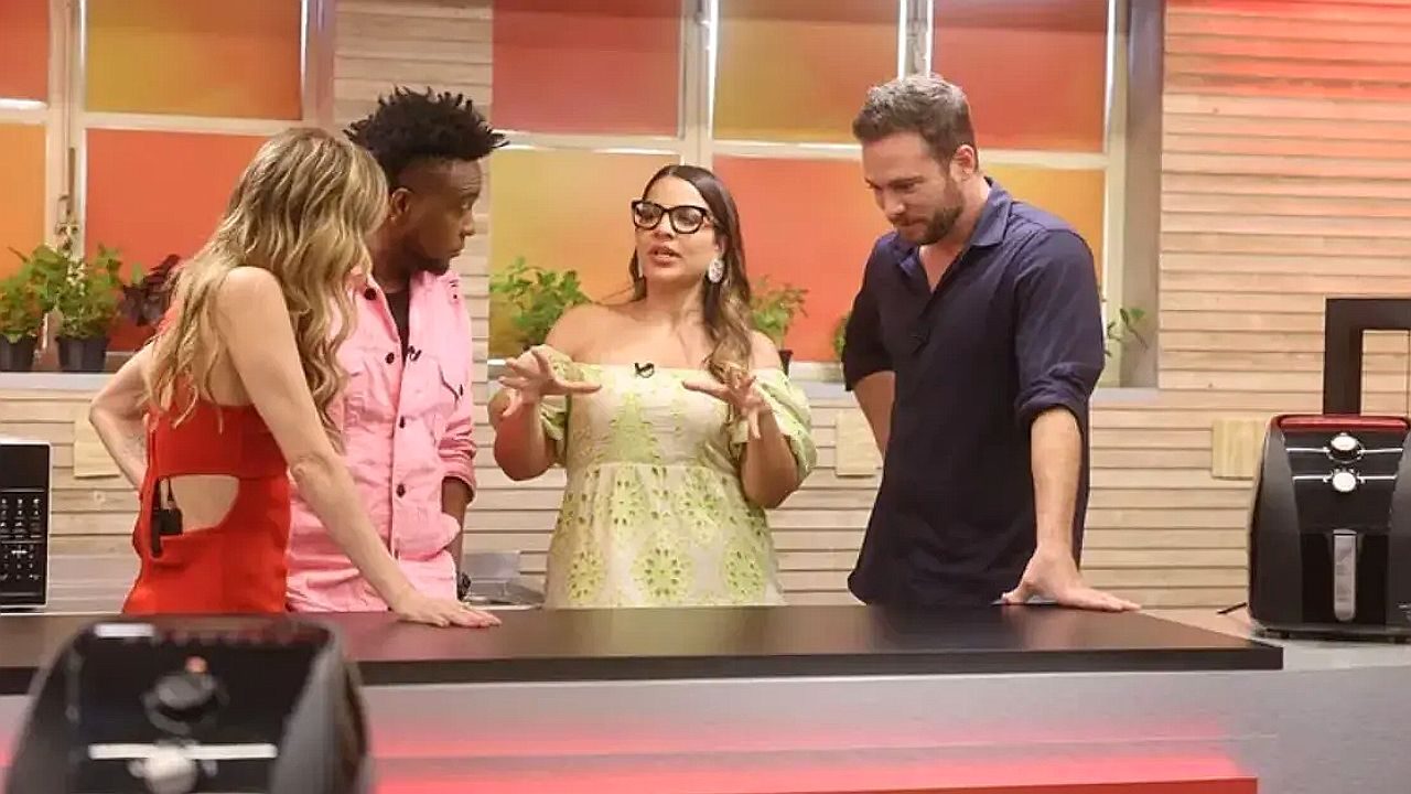 Quatro apresentadores conversam ao redor de bancada em programa de culinária na televisão