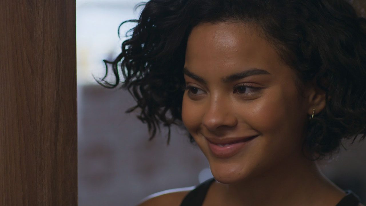 Maria de Fátima (Bella Campos) sorrindo em cena de Vale Tudo com fundo desfocado