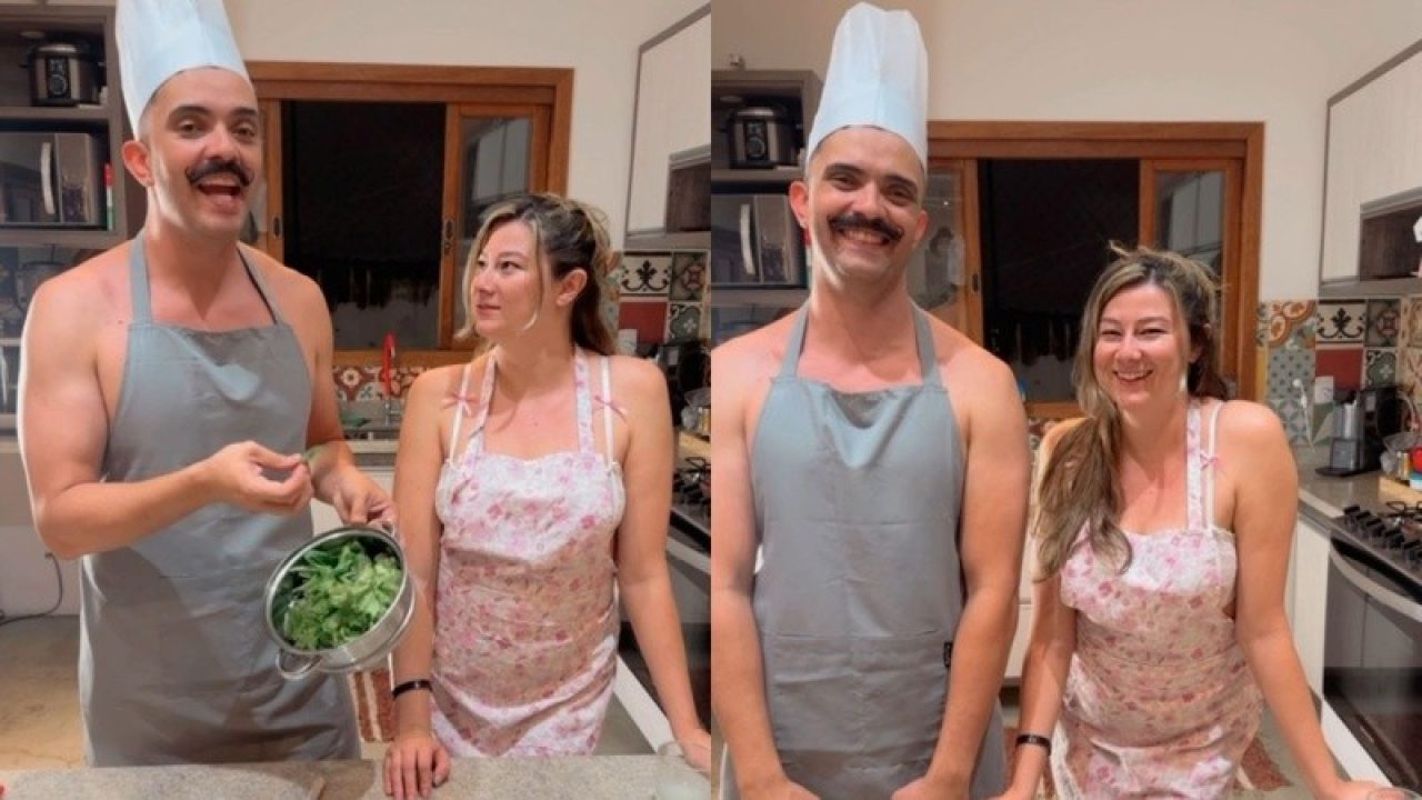 Bella Mantovani e Vagner Macedo em cozinha usando aventais e chapéu de chef enquanto preparam alimento e posam sorrindo