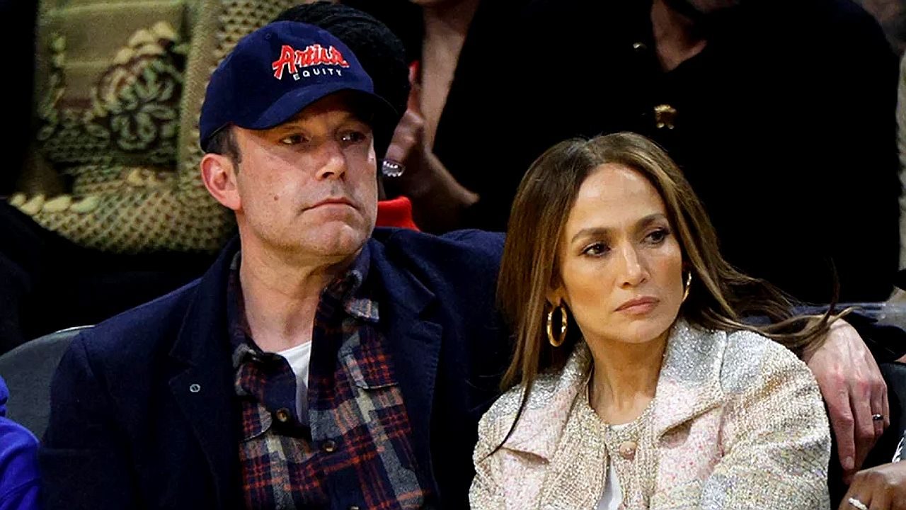 Homem de boné e mulher com brincos grandes assistem evento esportivo sentados na arquibancada