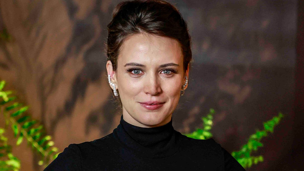 Bianca Bin com cabelo preso usa vestido preto de gola alta e brincos brilhantes posando diante de fundo desfocado