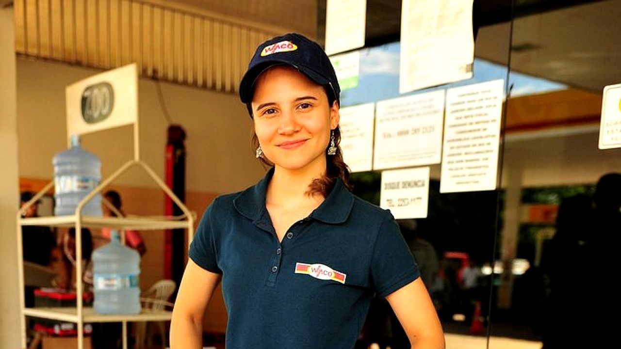 Funcionária de loja com uniforme e boné atende em frente a estabelecimento com avisos na porta