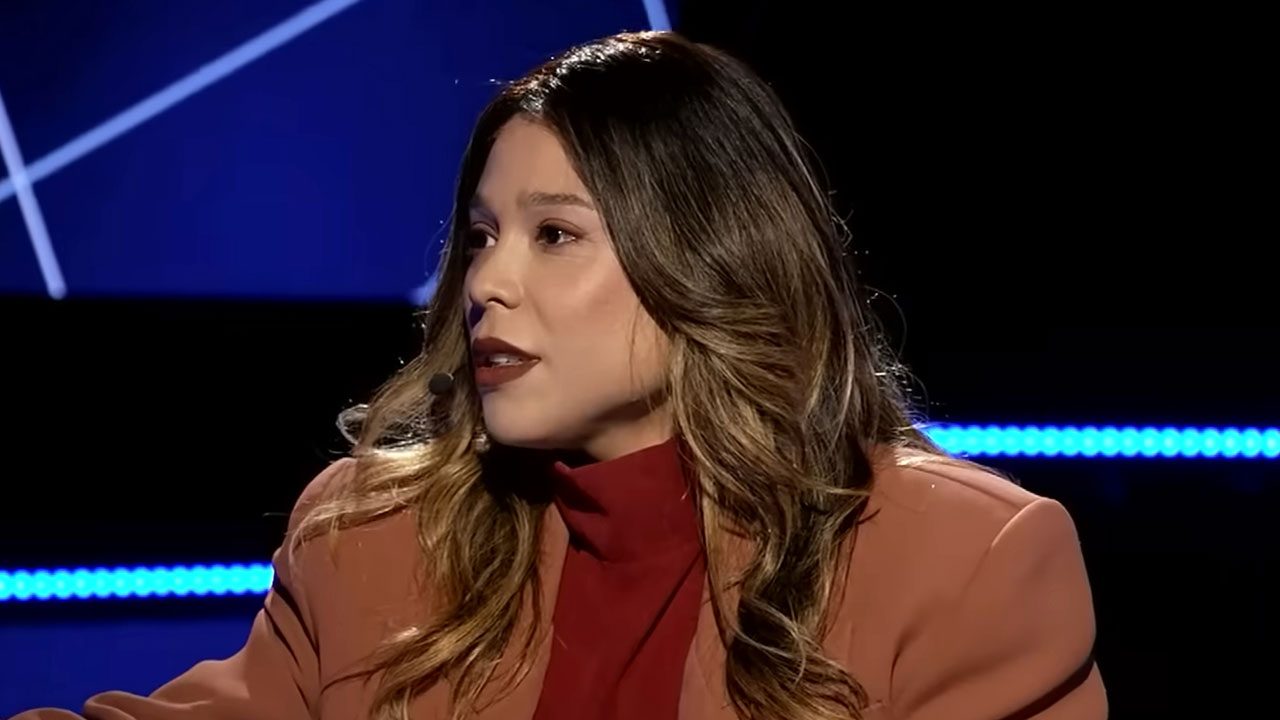 Blogueirinha veste blazer terracota e gola alta vinho enquanto fala ao microfone headset durante gravação de entrevista em estúdio