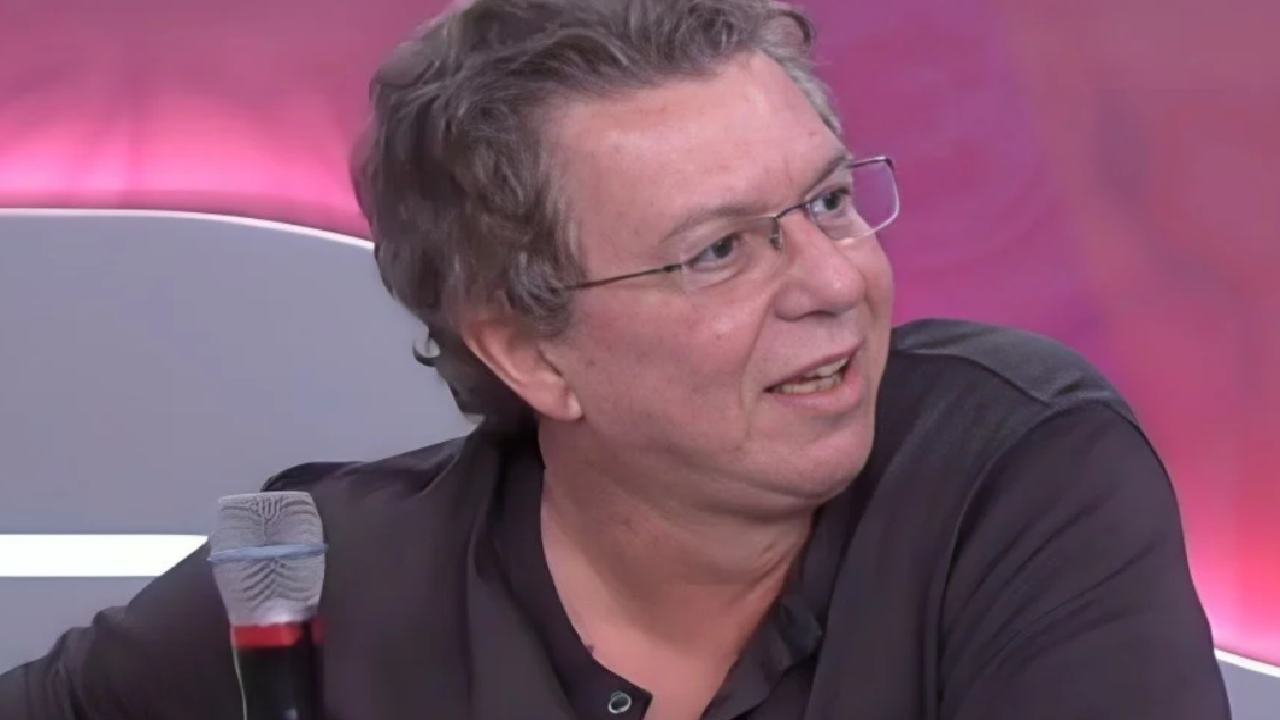 Boninho sentado em estúdio com microfone e fundo rosa iluminado