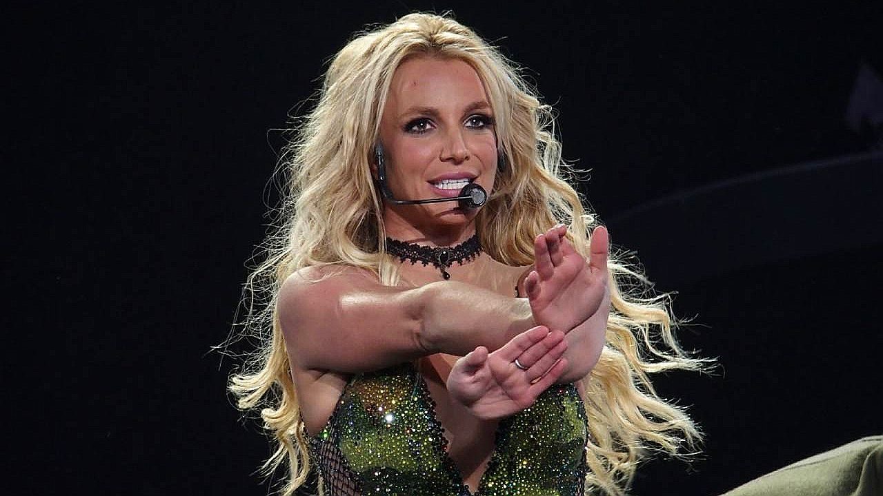 Britney Spears com microfone canta e faz gesto com as mãos durante apresentação no palco