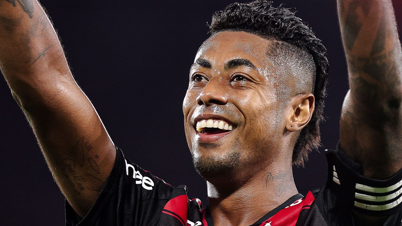 Bruno Henrique, jogador do Flamengo, sorrindo e com braços levantados celebrando em campo de futebol