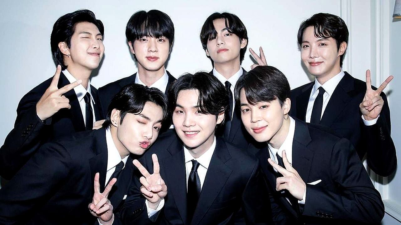Integrantes do BTS posam de terno preto fazendo sinal de paz em foto oficial do grupo de K-pop