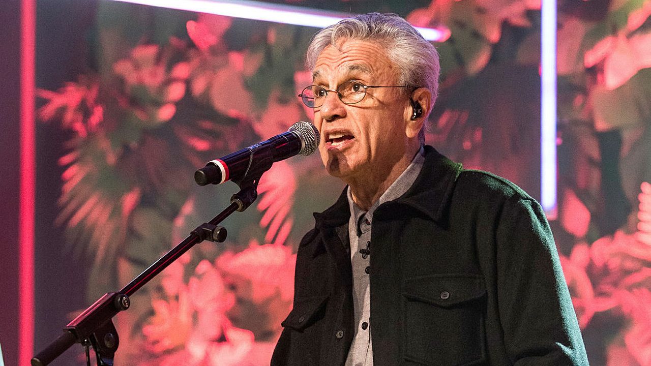 Caetano Veloso com óculos e fone de ouvido cantando em frente ao microfone no programa Conversa com Bial