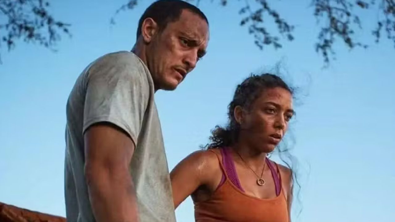 Cena da série Cangaço Novo, mostrando dois personagens cobertos de poeira e suor, com expressões cansadas e tensas, sob a luz do entardecer em uma paisagem árida do sertão