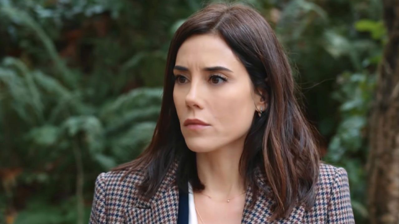 Cansu Dere com expressão séria usando blazer xadrez em cena da novela turca Iludida