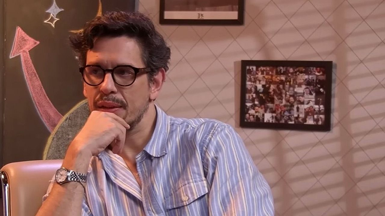 João Vicente de Castro com óculos e mão no queixo durante participação em programa de entrevistas