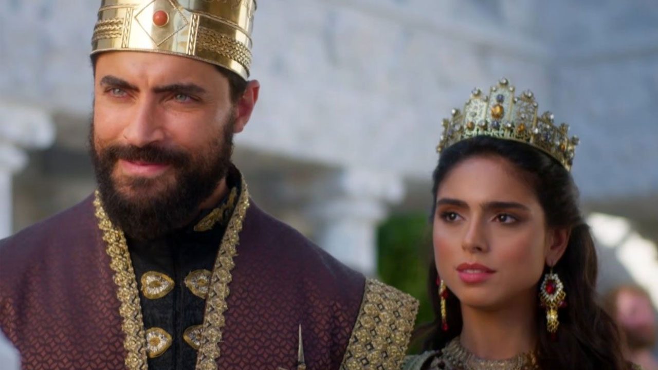 Carlo Porto como Xerxes e Nathalia Florentino como Ester usando coroas em cena da novela A Rainha da Pérsia