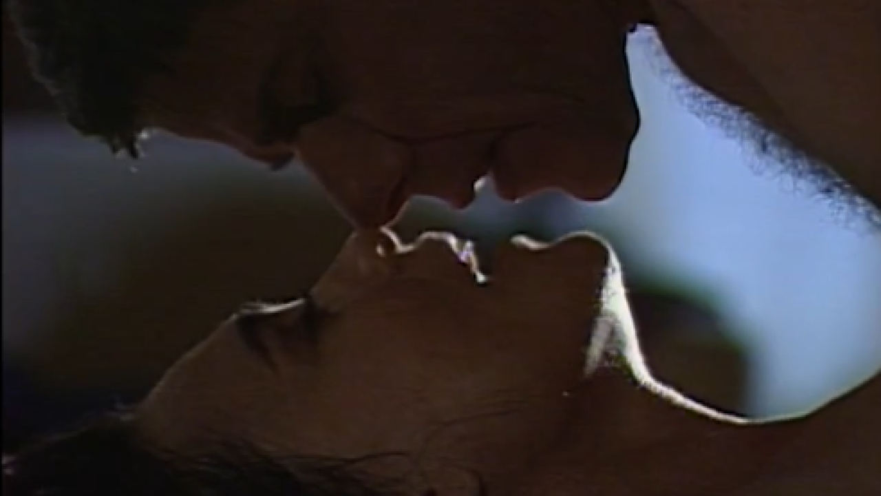 Cena romântica entre Helena e Carlos na novela História de Amor, com os personagens próximos e deitados em ambiente escuro.