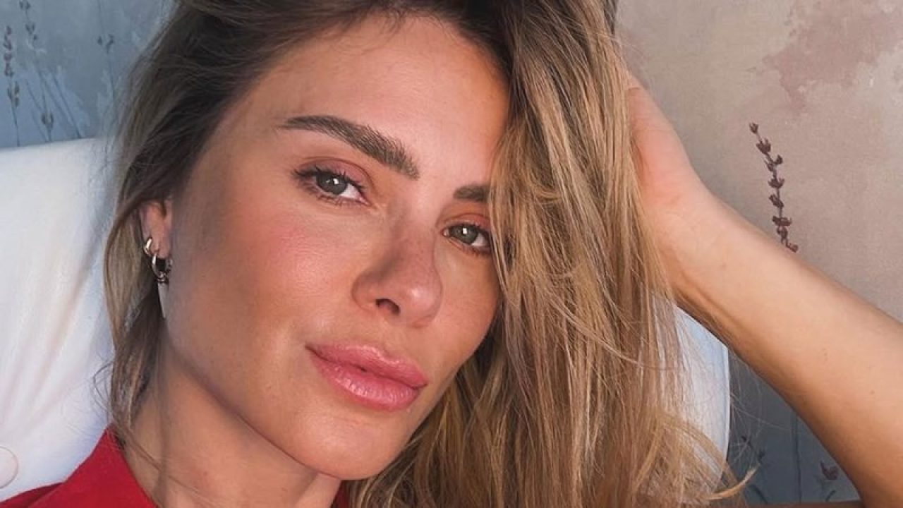 Carolina Dieckmann posa em um close natural, com expressão serena e olhar direto para a câmera. A atriz exibe maquiagem leve e batom rosado, com os cabelos soltos e levemente despenteados, apoiando uma das mãos na cabeça. A iluminação suave valoriza os traços da artista em um ambiente de fundo neutro e delicado.