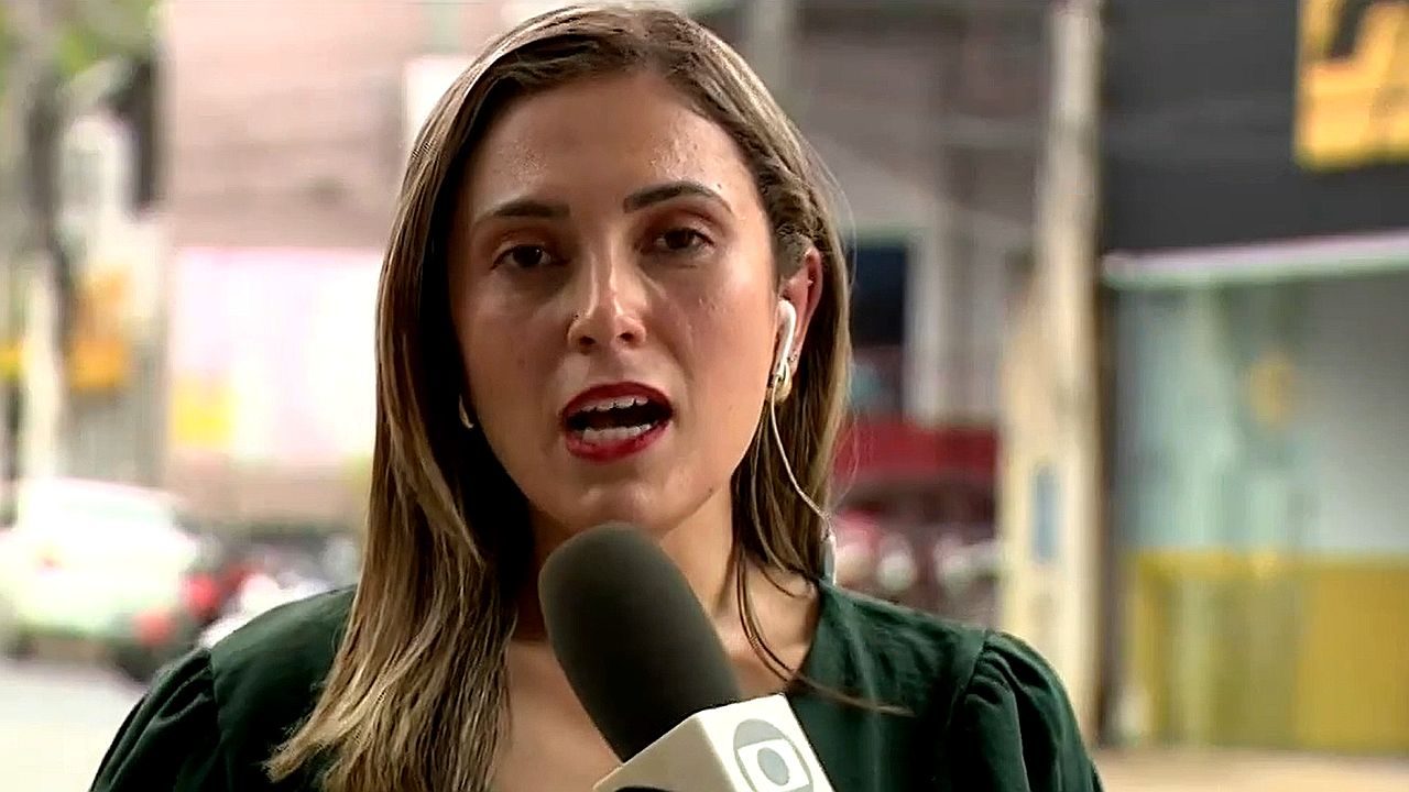 Mulher com microfone e fone de ouvido faz entrada ao vivo em reportagem de rua com carros ao fundo