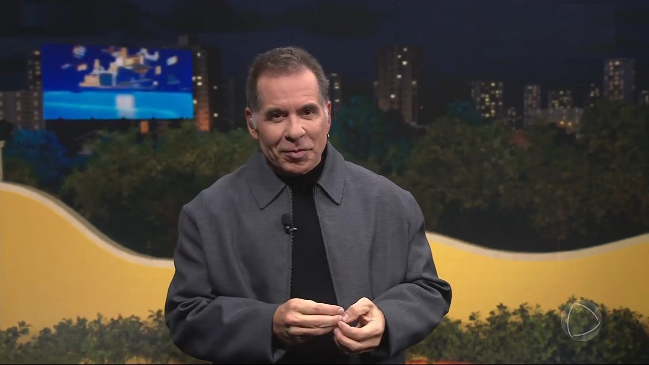 Leandro Hassum fala ao vivo na Casa do Patrão, reality show da Record, com cenário noturno e cidade iluminada ao fundo.
