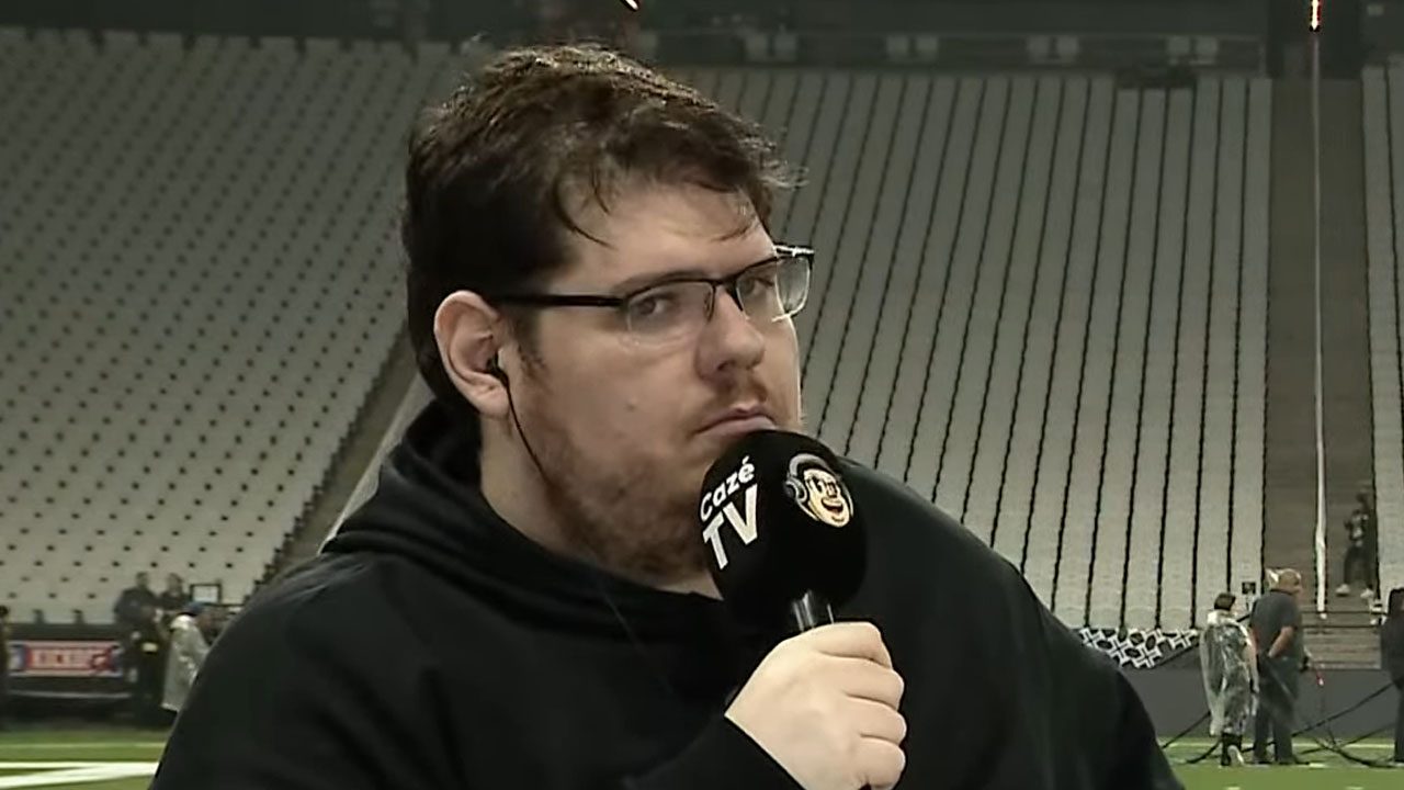Casimiro Miguel segurando microfone da Cazé TV durante transmissão em estádio vazio
