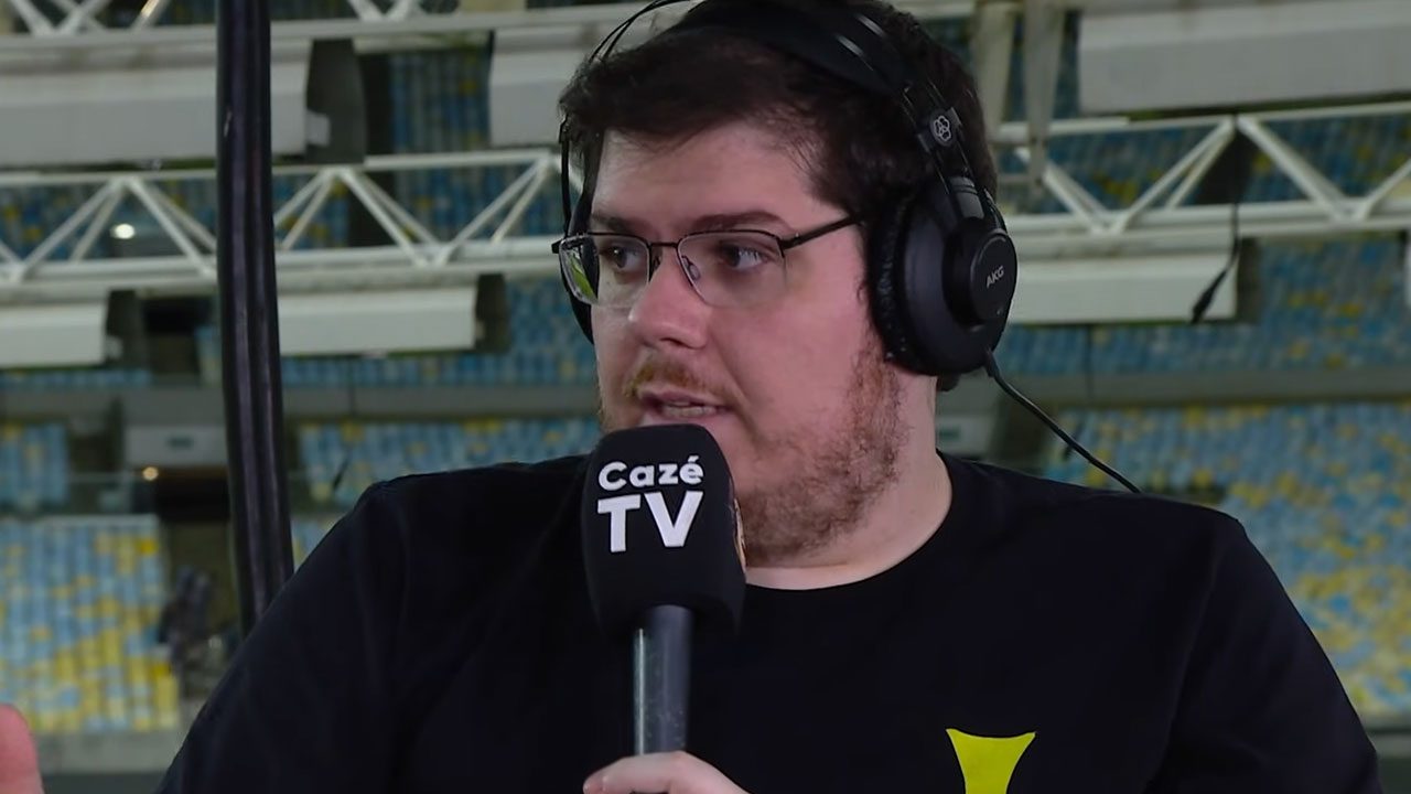 Casimiro Miguel com fone de ouvido segurando microfone da Cazé TV durante transmissão esportiva