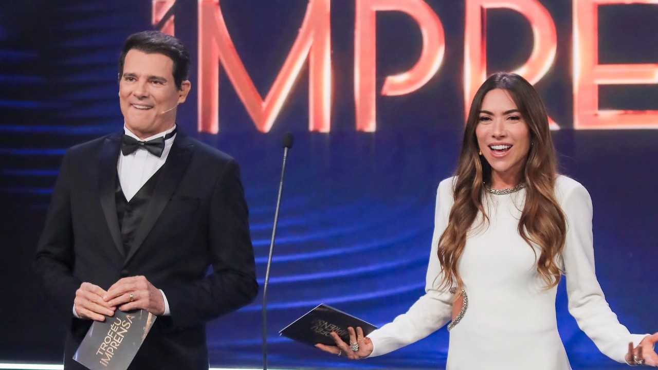Celso Portiolli de terno e Patricia Abravanel de vestido branco apresentam o Troféu Imprensa em palco iluminado