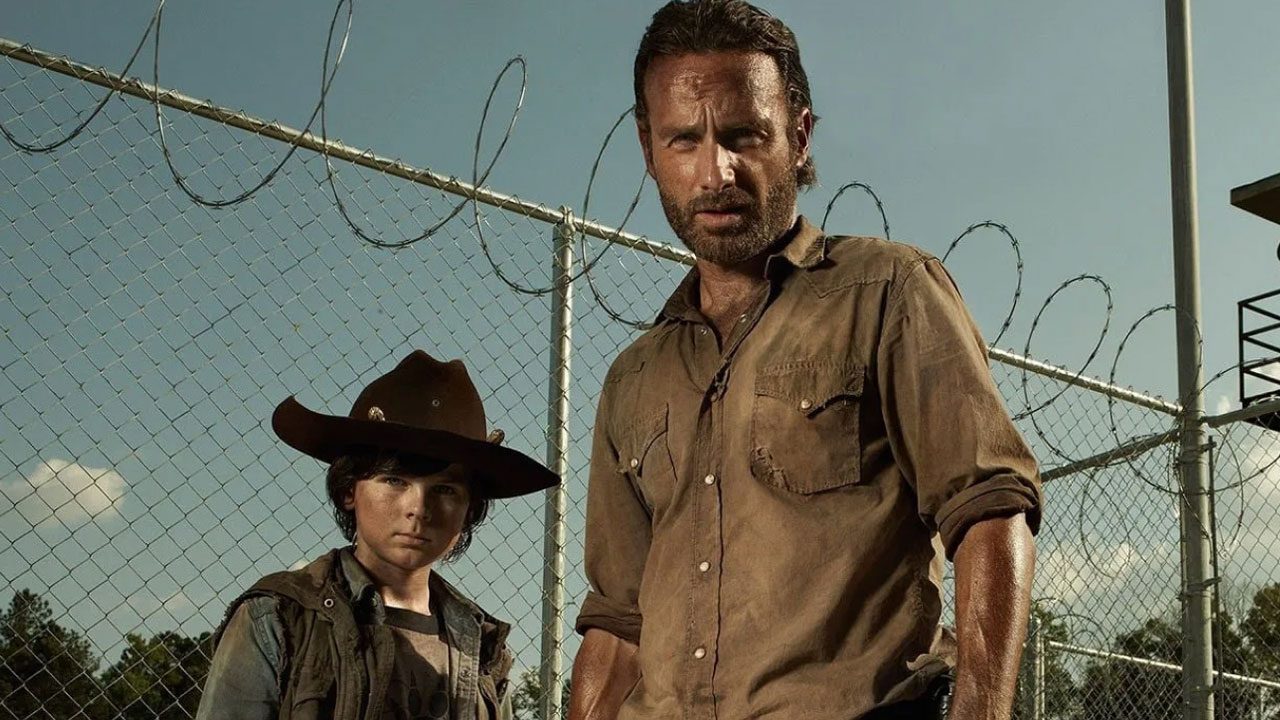 Carl Grimes e Rick Grimes diante de cerca de arame farpado em foto promocional da série The Walking Dead