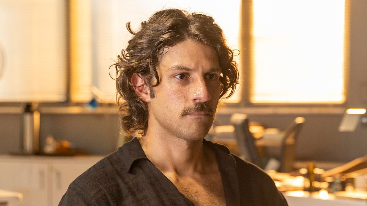 Chay Suede caracterizado como Mavi na novela Mania de Você com expressão séria em ambiente iluminado