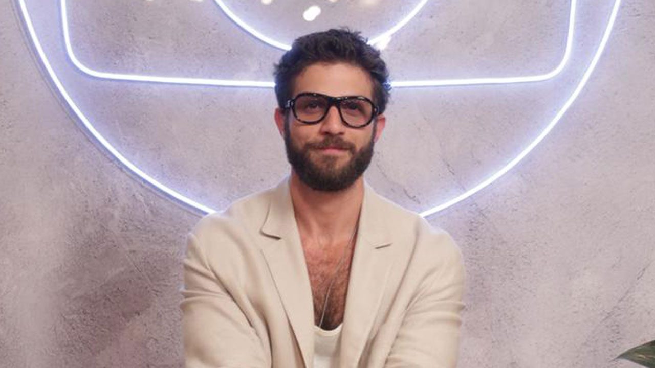 Chay Suede com barba, blazer e camiseta bege, usando óculos de armação escura, em evento da Globo