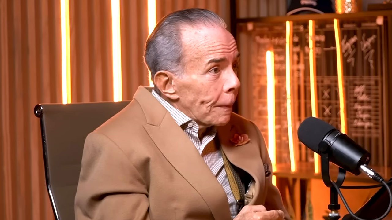 O empresário Chiquinho Scarpa, de terno bege e cabelo grisalho, fala em um microfone de estúdio durante participação em um podcast