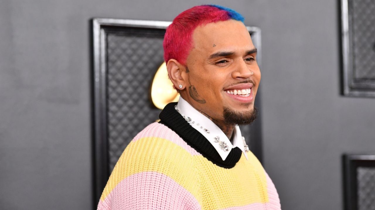 Chris Brown sorri com cabelo rosa e azul durante aparição em tapete vermelho de premiação musical