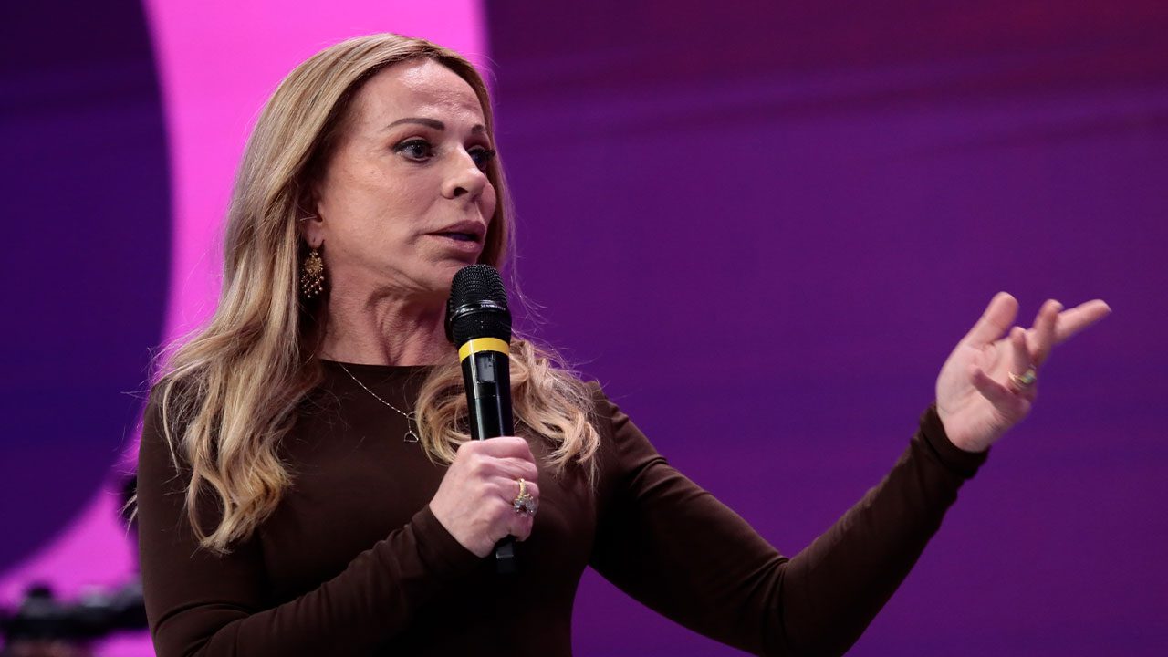 Christina Rocha segurando microfone e gesticulando durante coletiva sobre o Casos de Família em fundo roxo iluminado