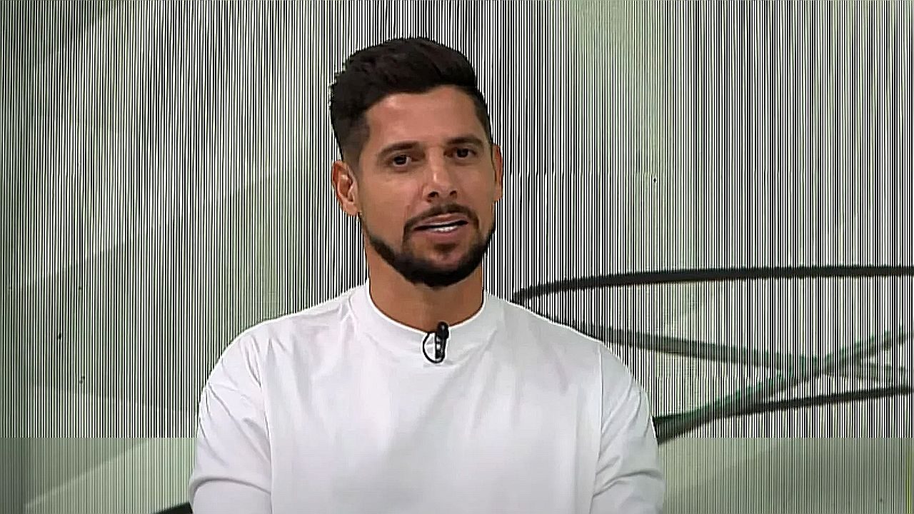 Apresentador de camiseta branca fala em estúdio de TV com microfone de lapela preso à roupa
